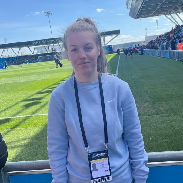 Photo of a white woman with blonde hair standing pitchside