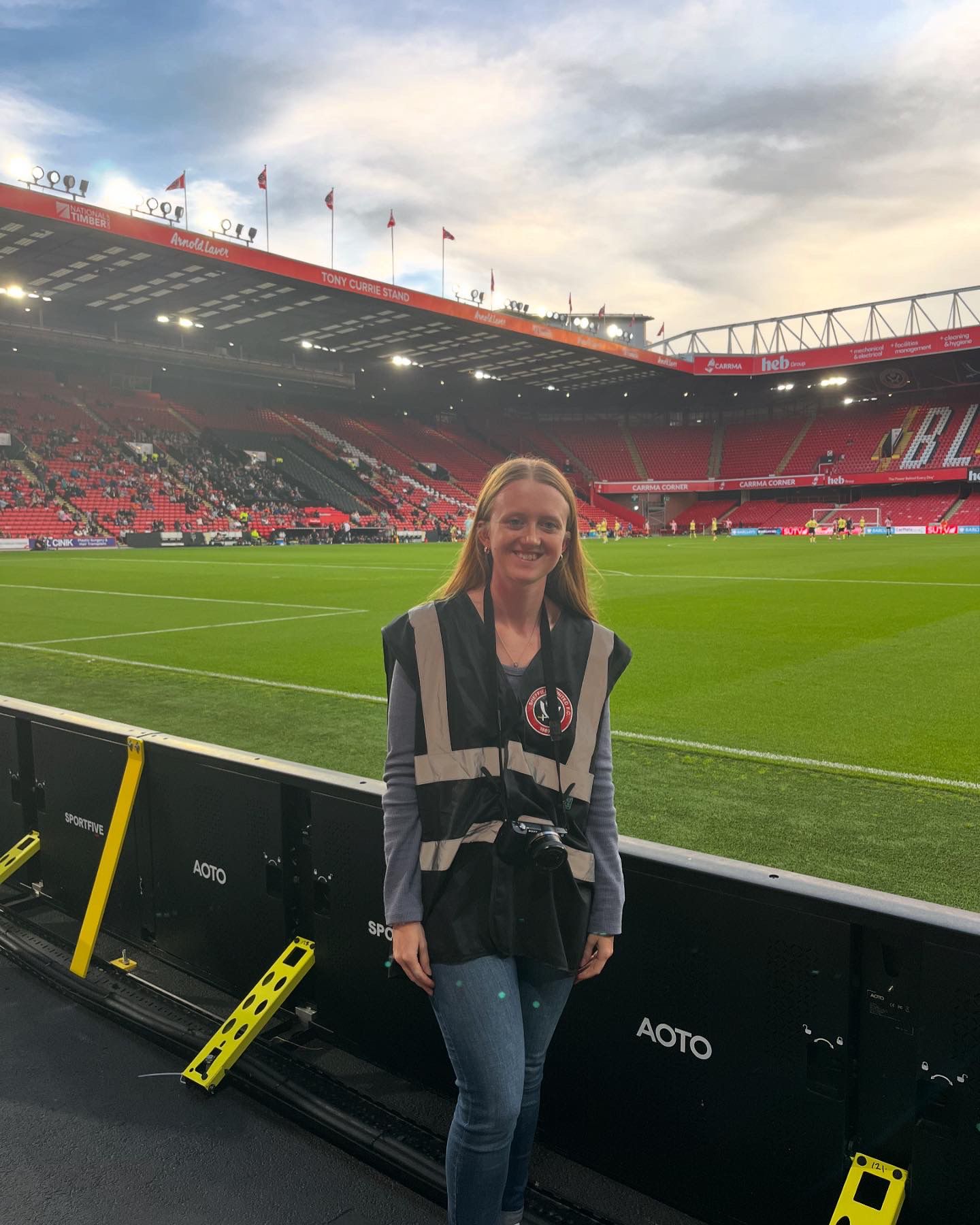 Photo of a white woman with blonde hair standing pitchside at a football stadium