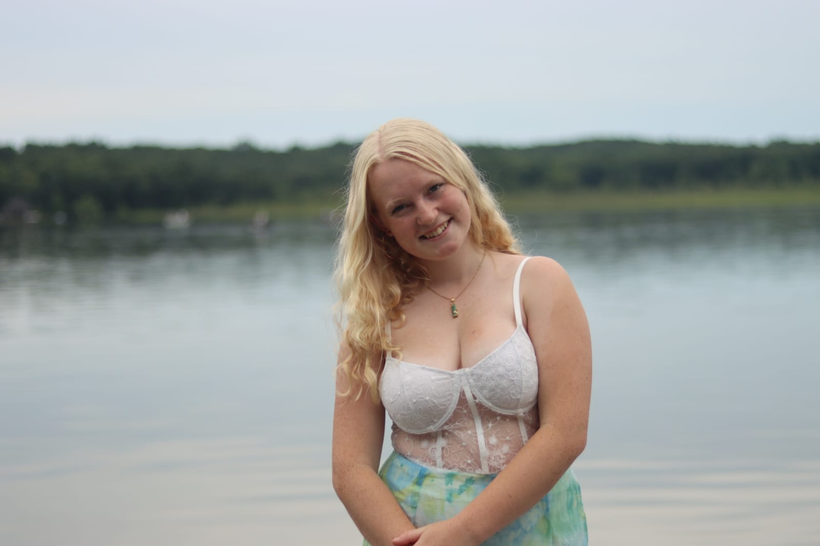 Photo of a white woman with blonde hair wearing a white lace top standing in front of a lake