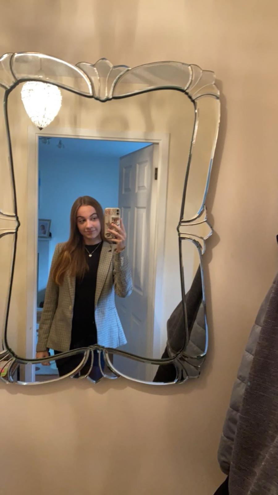 Mirror selfie of white woman with light brown hair wearing a black top and grey blazer