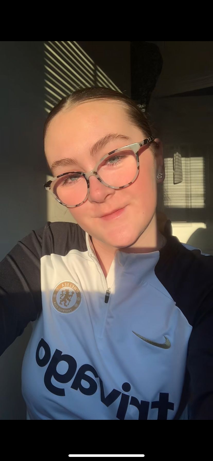 Photo of a White woman with Brown hair in a ponytail and black glasses. She is wearing a Chelsea Jumper