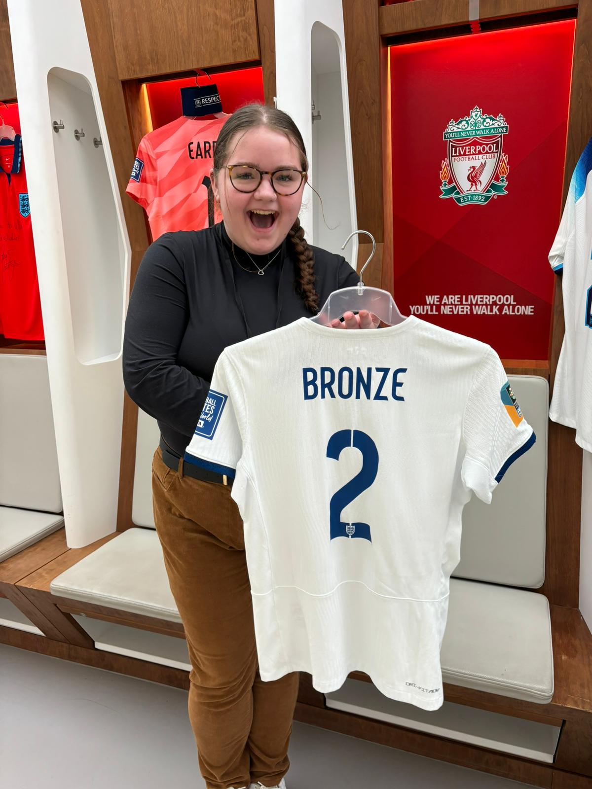 Photo of white woman with glasses smiling holding a Lucy Bronze England shirt
