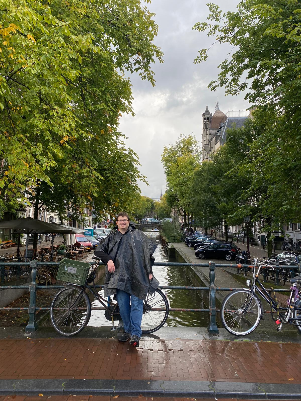 Photo of white man wearing ginormous anorak standing on bridge over canal