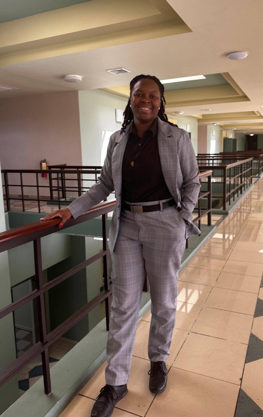 Photo of black woman wearing a grey suit smiling standing in front of staircase