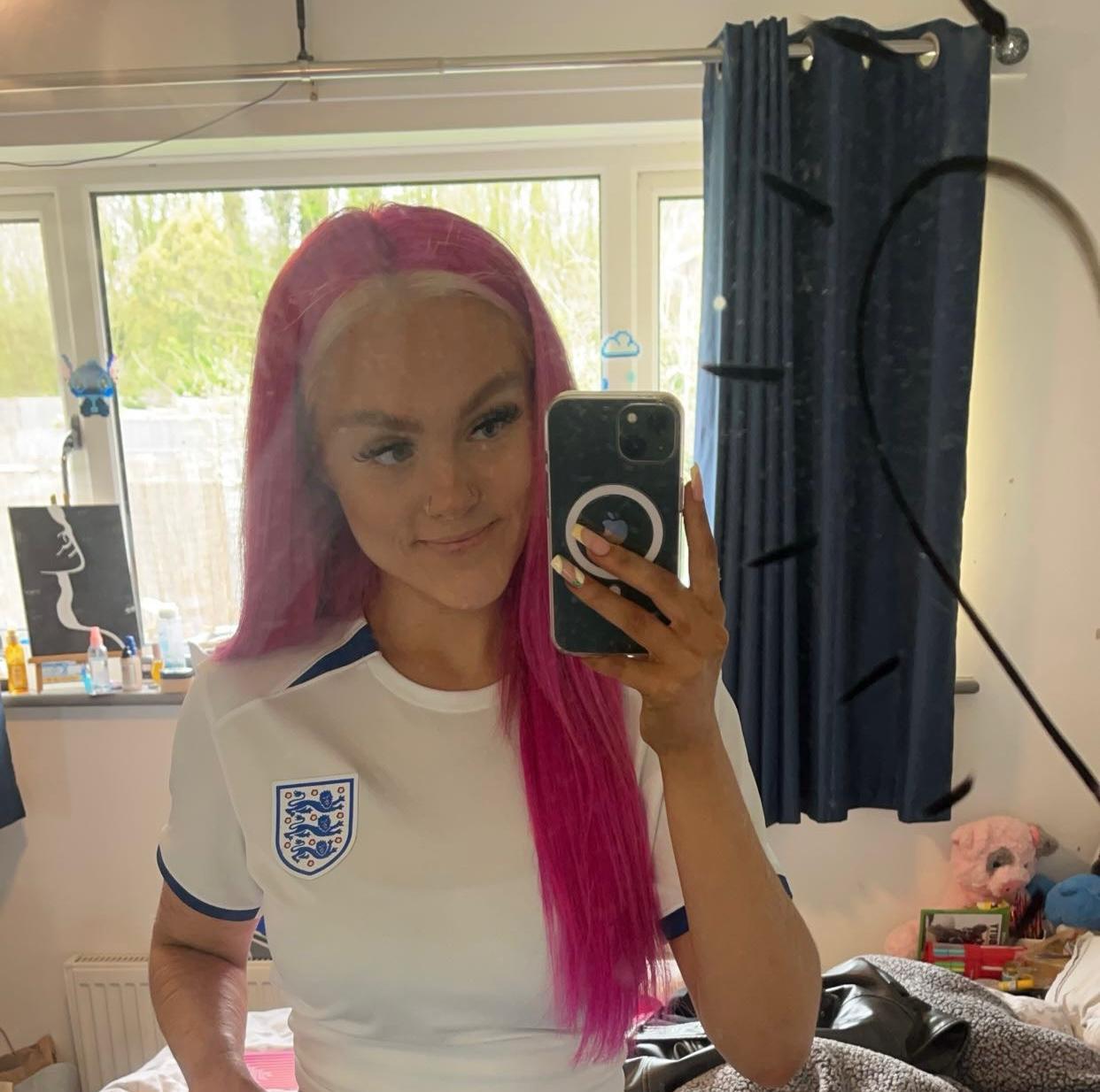 Photo of white woman with bright pink hair wearing an England football kit
