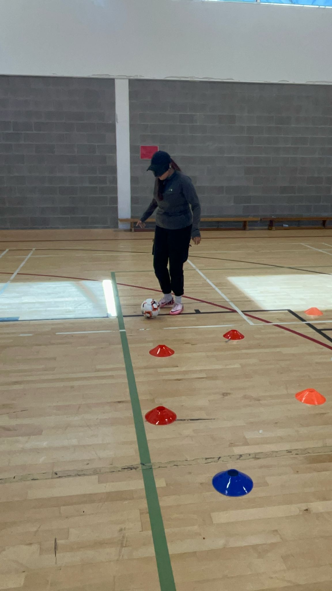 Nailah playing football, dribbling round some cones.