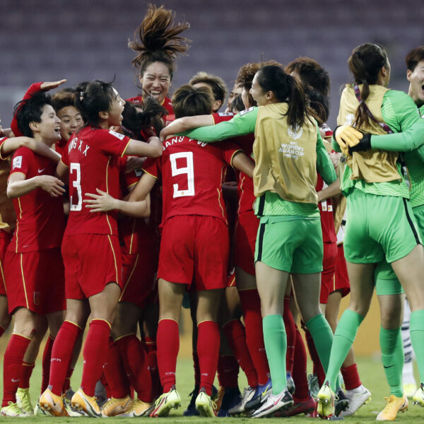 China's Women’s national team players in red kits celebrating together in a large huddle on the pitch, smiling and embracing while two goalkeepers in green hug on the side during the post-match celebration.