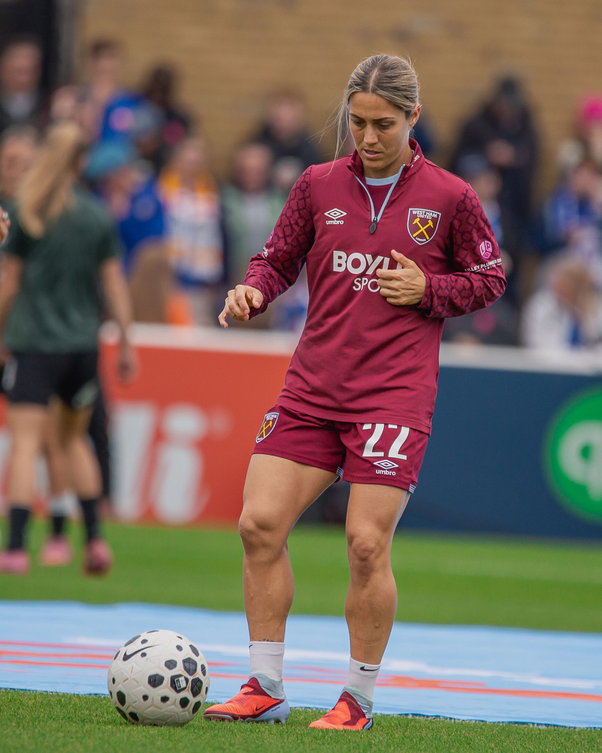West Ham United midfielder Katrina Gorry controls the ball during a warm-up on the pitch, wearing the club’s claret home kit.