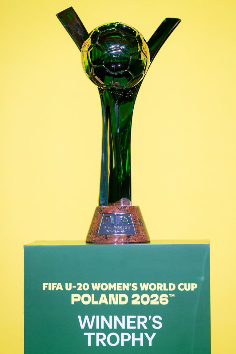 The FIFA U-20 Women’s World Cup Poland 2026 winners’ trophy displayed on a green plinth against a bright yellow background.
