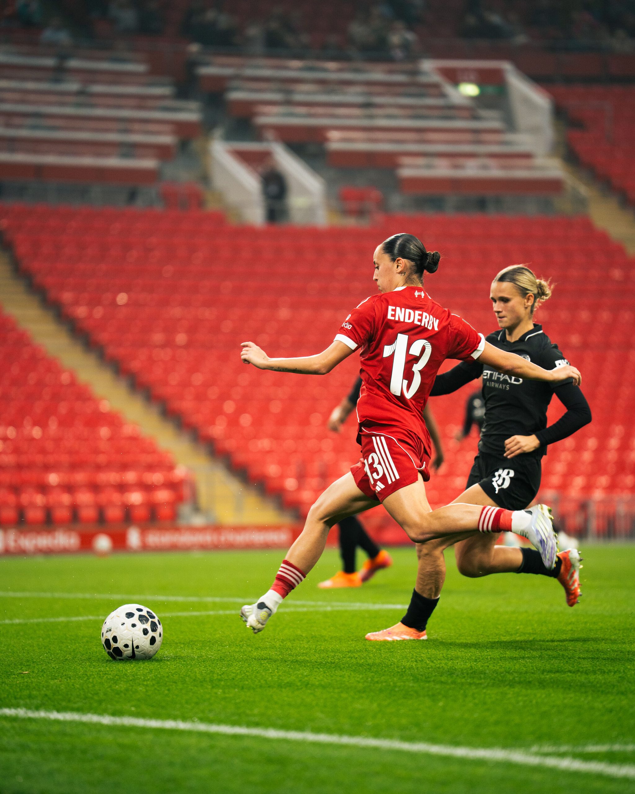 Liverpool Women forward Mia Enderby strikes the ball while under pressure from a Manchester City player during a match at Anfield.