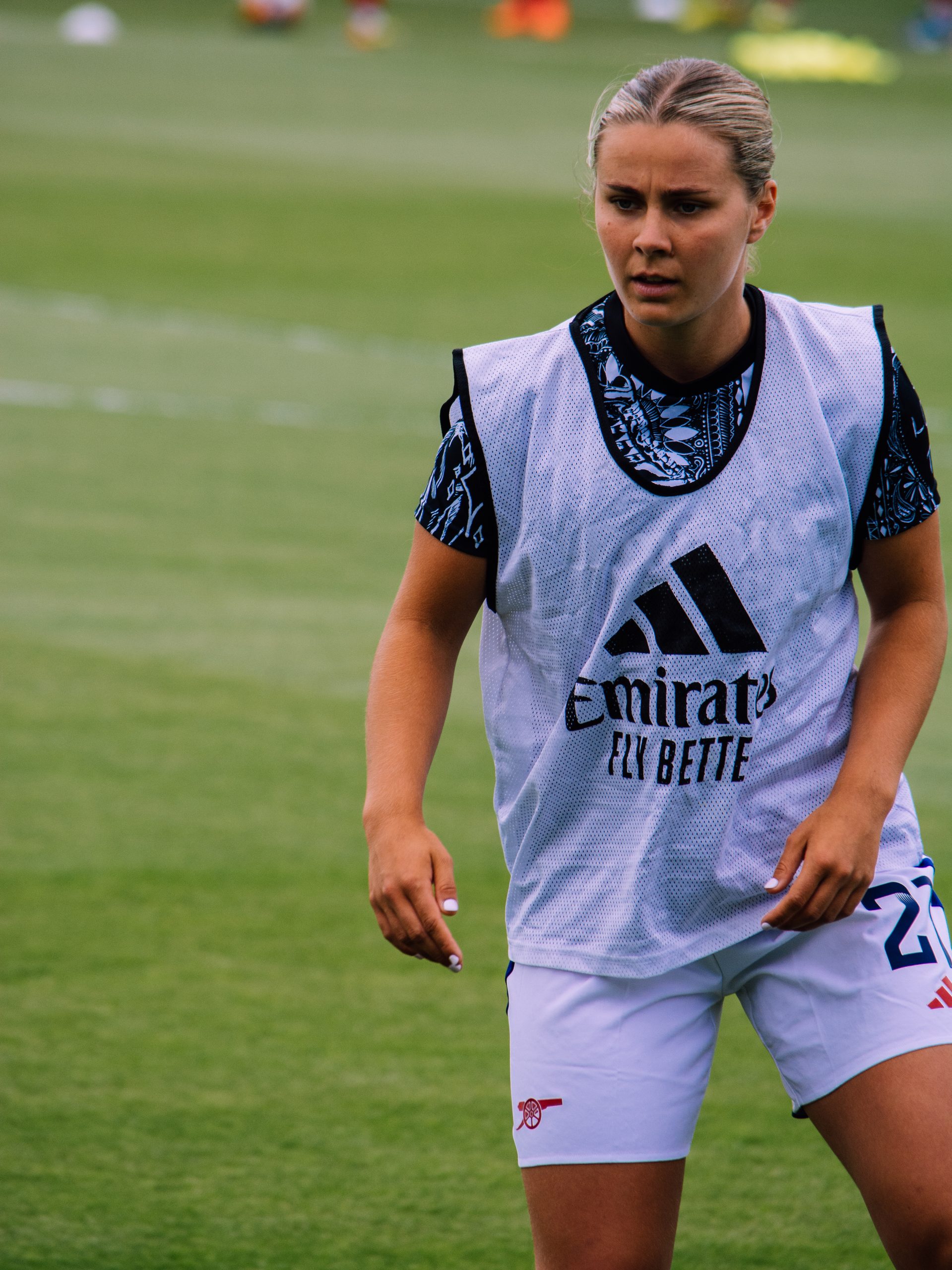 Victoria Pelova wearing a white training bib over a black-and-blue patterned training shirt and white shorts, pictured on the pitch during a warm-up.